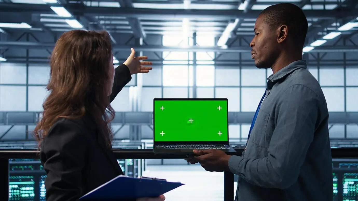 Инженеры в центре обработки данных, используя ноутбук с зелёным экраном, проверяют состояние оборудования.