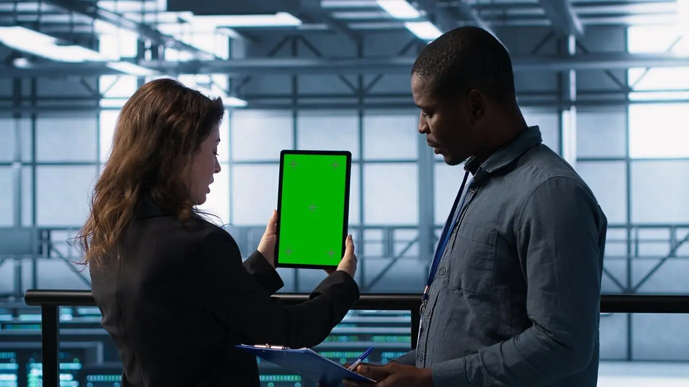 Техники в дата-центре проверяют оборудование, используя планшет с зелёным экраном.